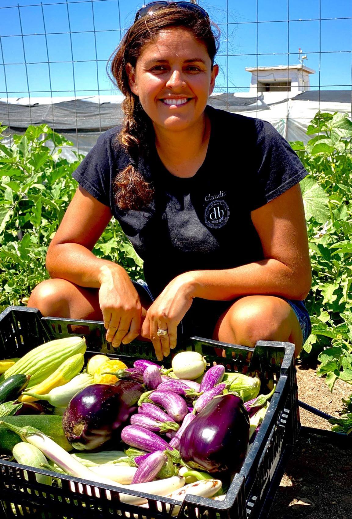Claudia holding a summer harvest of eggplants, squash, and cucumbers in the EU garden.